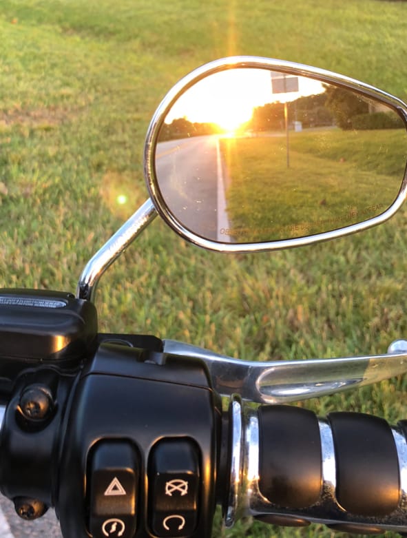 A photo of a bike mirror showing the setting sun in the mirror